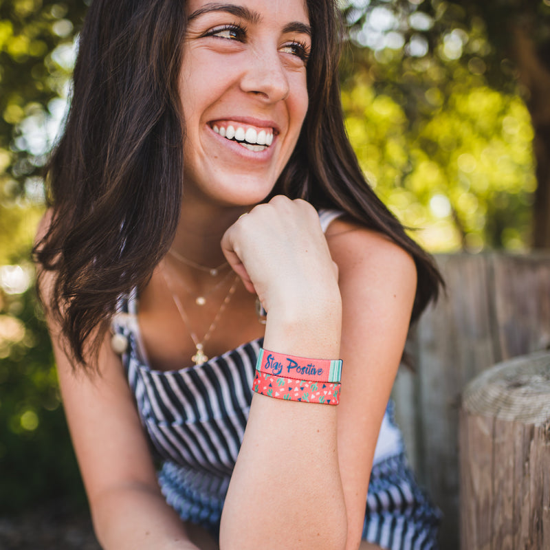 Lifestyle image close up of someone smiling with 2 Stay Positive on their wrist 