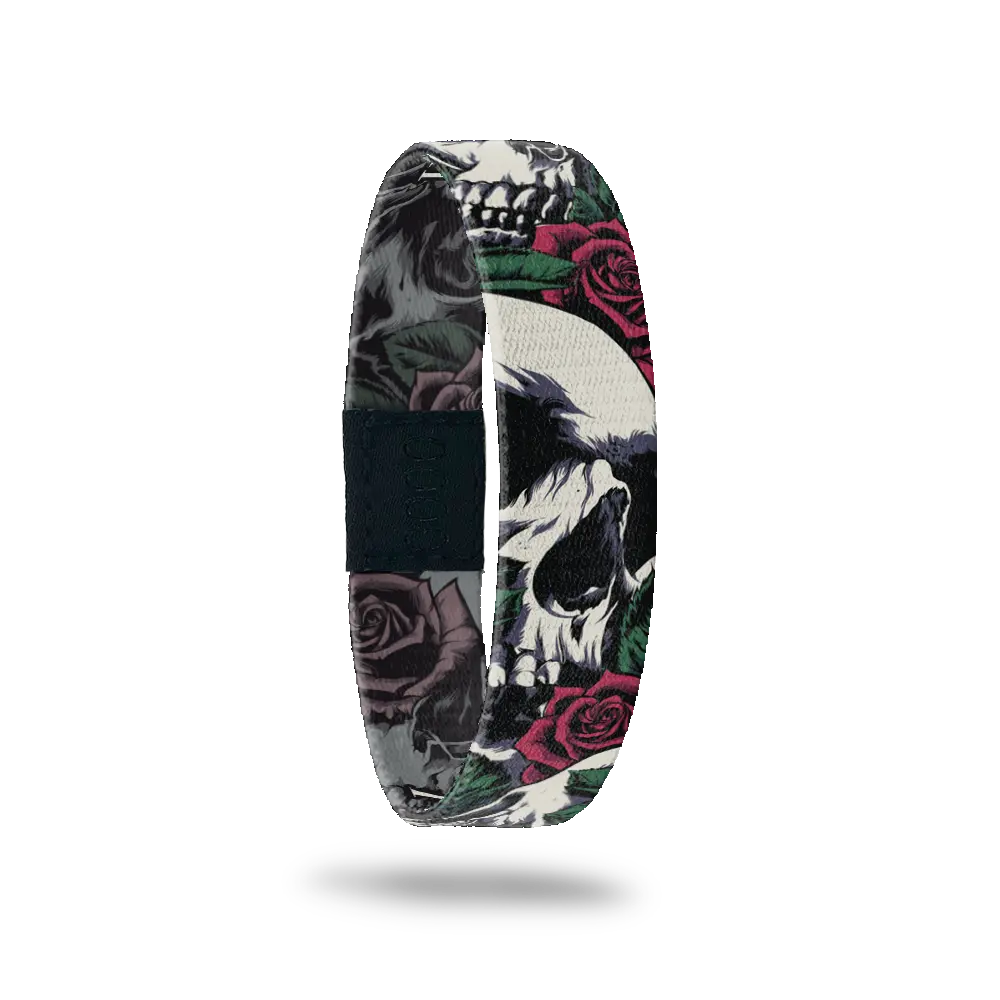 Wristband single with a design of white and grey skulls up close intertwined in roses and leaves; very grunge looking. The inside is the same design except in all black and white and reads Memento Mori. 