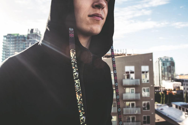 Young Adult male with hood up switching out the interchangeable strings from one design to another with a city skyline in the back 