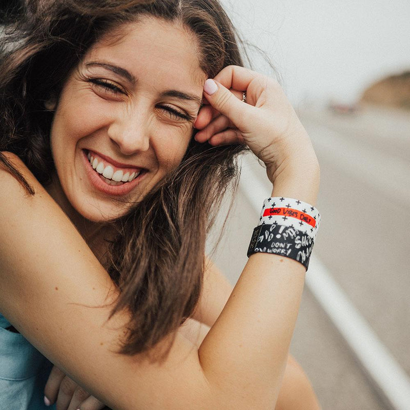 Lifestyle image of woman resting on a railing with arm wearing 2 Good Vibes Only straps