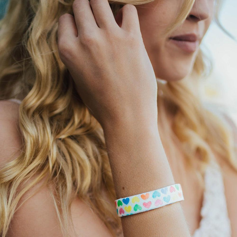 Lifestyle photo up close of girl showing wrist with live with love single showing the outside design of with rows of pastel orange, yellow, pink, green, purple, and blue gradient hearts over white background