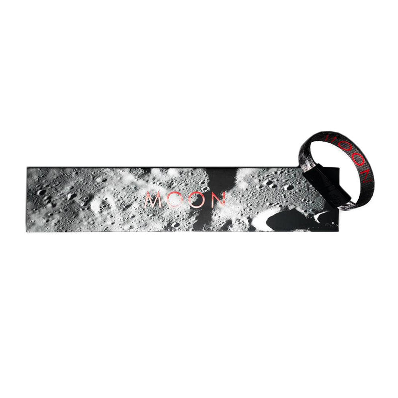 Studio image of Moon clasped together laying on the box it comes in, which has a design of a realistic grey image of the moon's surface and Moon centered in red text