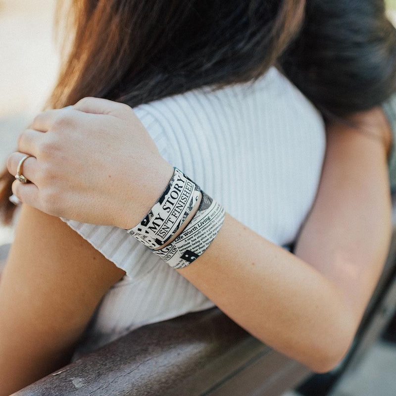 Lifestyle image of someone resting their head and arm around someone else's shoulder and wearing 2 My Story Isn't Finished wristbands