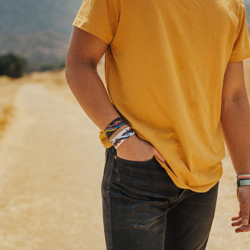 lifestyle image of a man with his hand in his pocket with two make your own path wristbands on. One showing the outside design and one showing the inside.