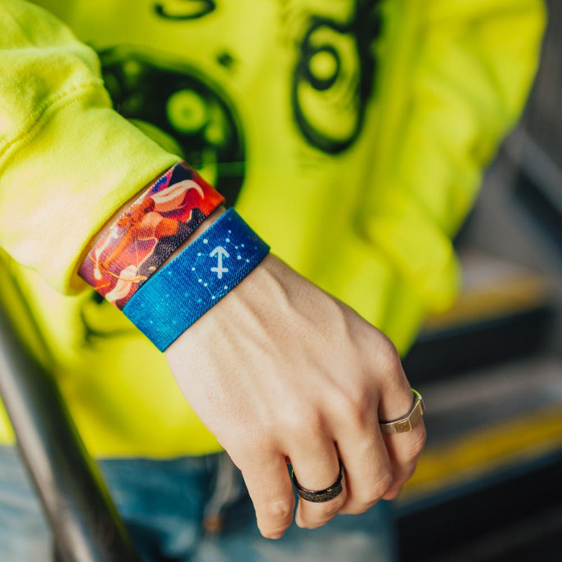 Lifestyle close up image of arm resting on a railing and two Sagittarius straps on their wrist