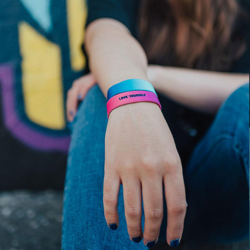 Lifestyle photo of a girl resting wrist on knee displaying the outside design of begin again and the inside design of love yourself showing a small bold black text love yourself overlaying a purple to pink gradient