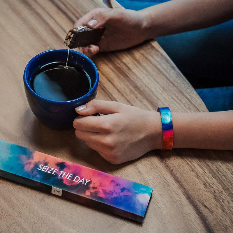 Lifestyle image of someone having coffee and a biscuit wearing Seize The Day with it's box on the table next to the coffee