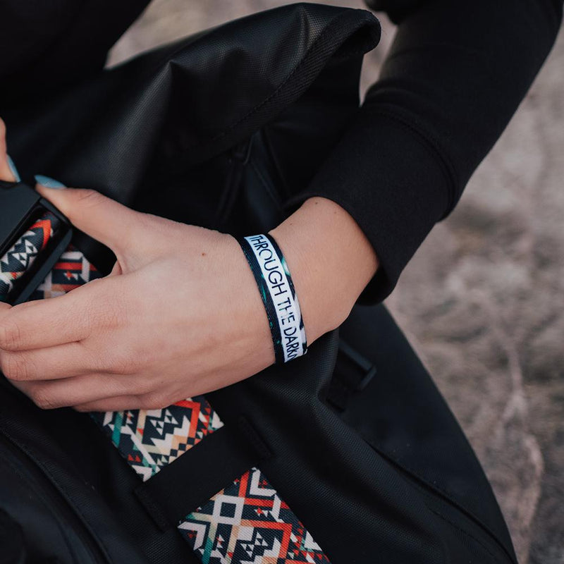 Lifestyle image of someone holding their bag with Through The Darkness on their wrist