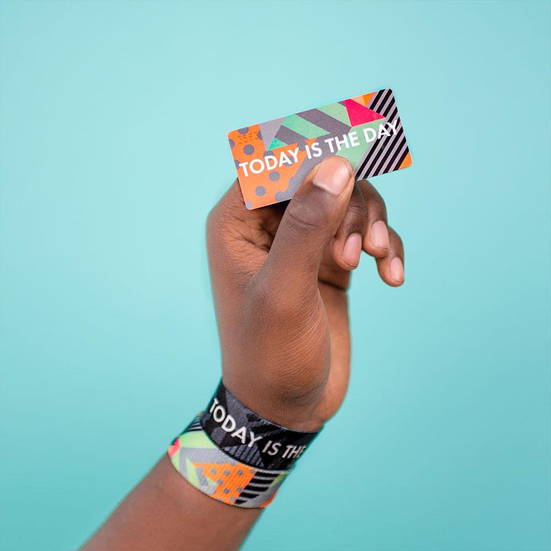 Studio image of hand holding a card that says Today Is The Day and wearing 2 Today Is The Day on their wrist