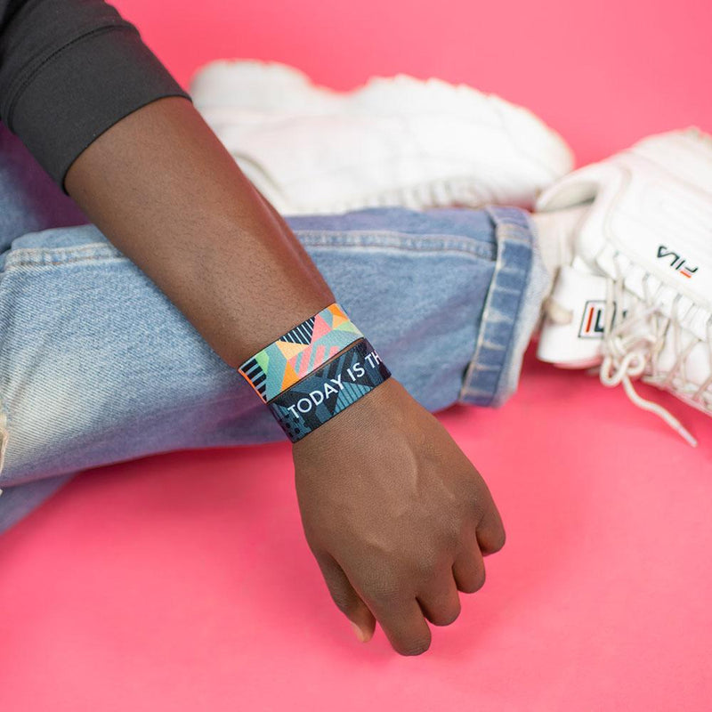 Studio image of model sitting with arm resting on leg wearing 2 Today Is The Day on their wrist 