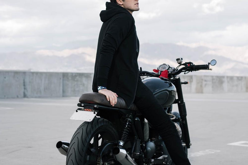 a young adult male sitting on a motorcycle showing a side view of the black zipper imperial hoodie