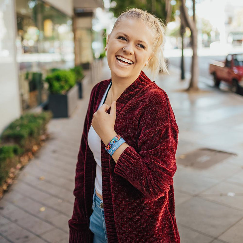 A woman wearing two You're Going To Be Okay at once. Once shows the inside while one shows the outside. Her hand is on her sweater collar