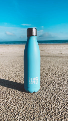 blue-stainless-steel-waterbottle-upright-on-sand-gym-plus-coffee-resuable-water-bottle