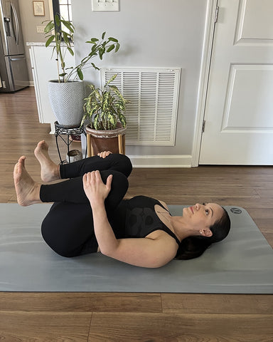 Daniela Spear deep breathing while doing a knee hug on her yoga mat