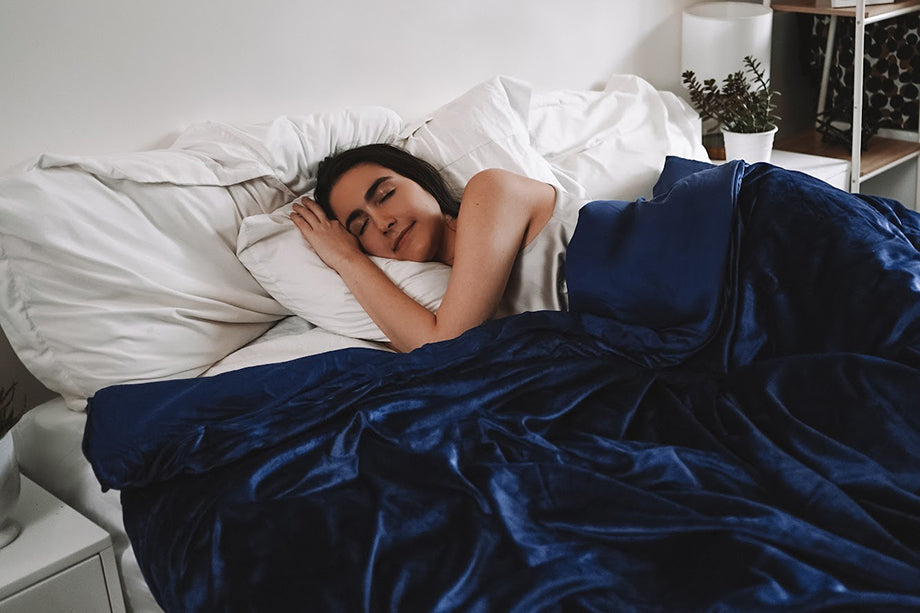 a woman sleeping in bed under a blue weighted blanket