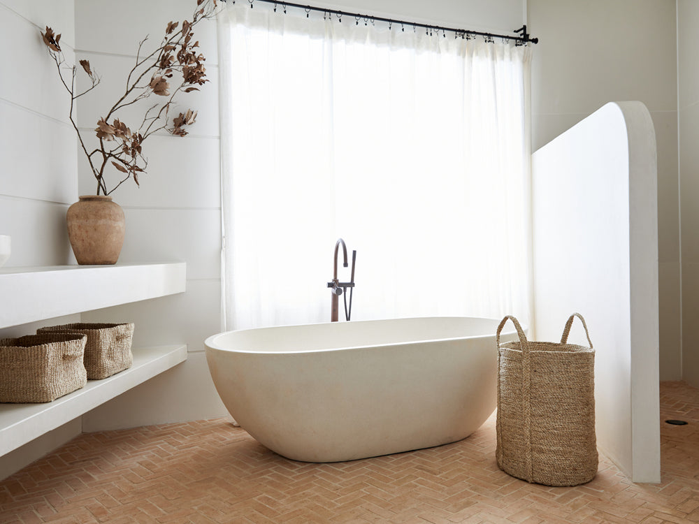 Fair trade storage baskets and laundry hampers in a neat bathroom with white curtains.