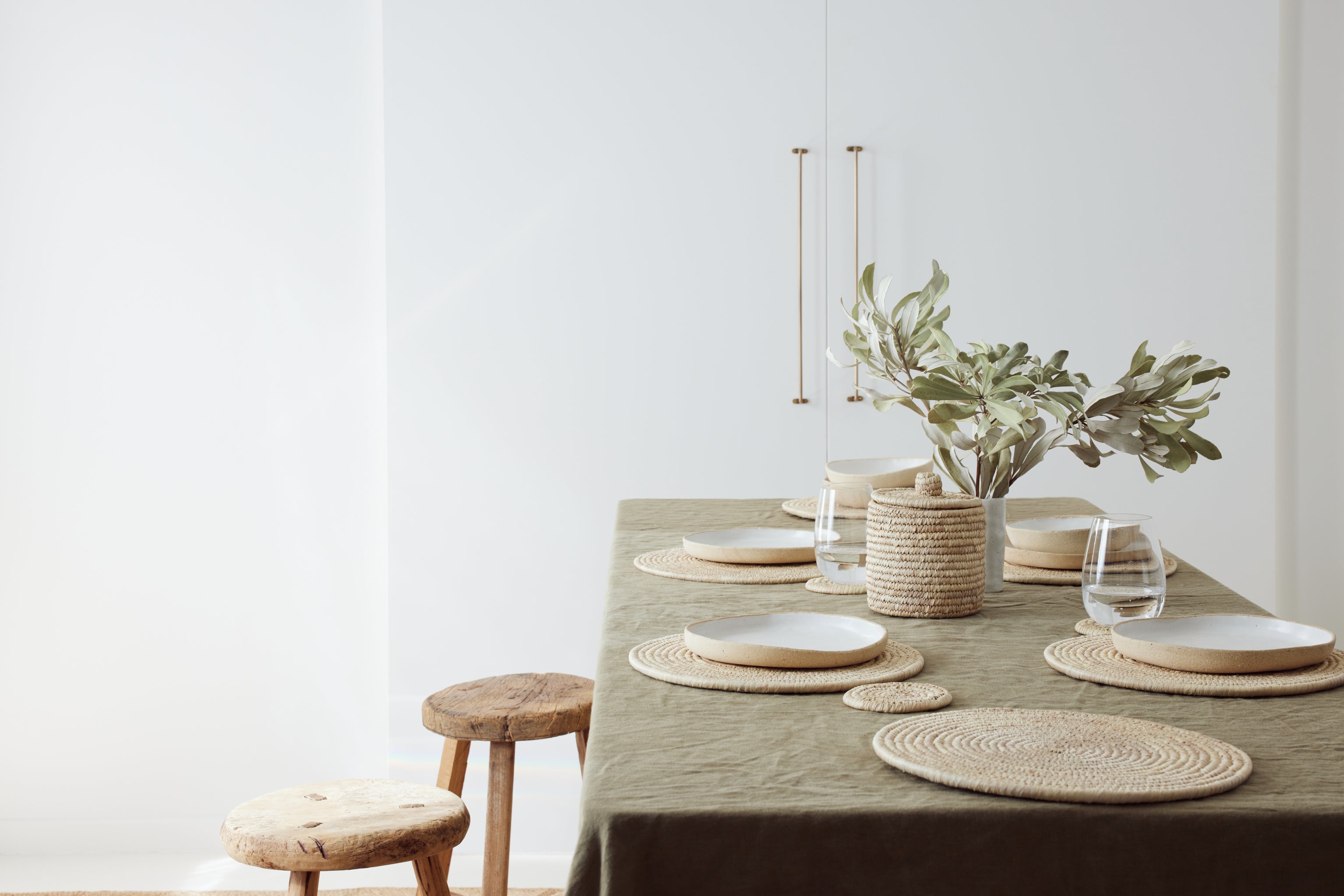 table setting with palm fibre placemats, olive green linen and foliage