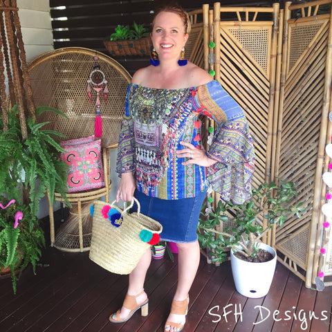 lady standing on a balcony holding a bag dressed in denim skirt and boho top