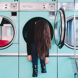 Girl inside of a front-load washing machine with long hair covering face. Her head, arms and feet hang outside open door.