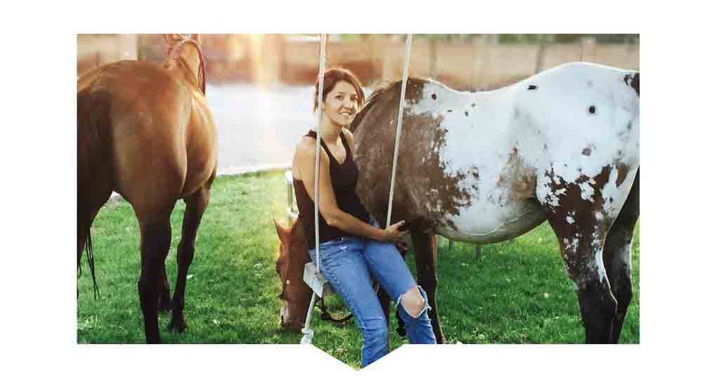 Speech Therapist Tanya Friend sitting on a swing next to her two horses with water in the background.