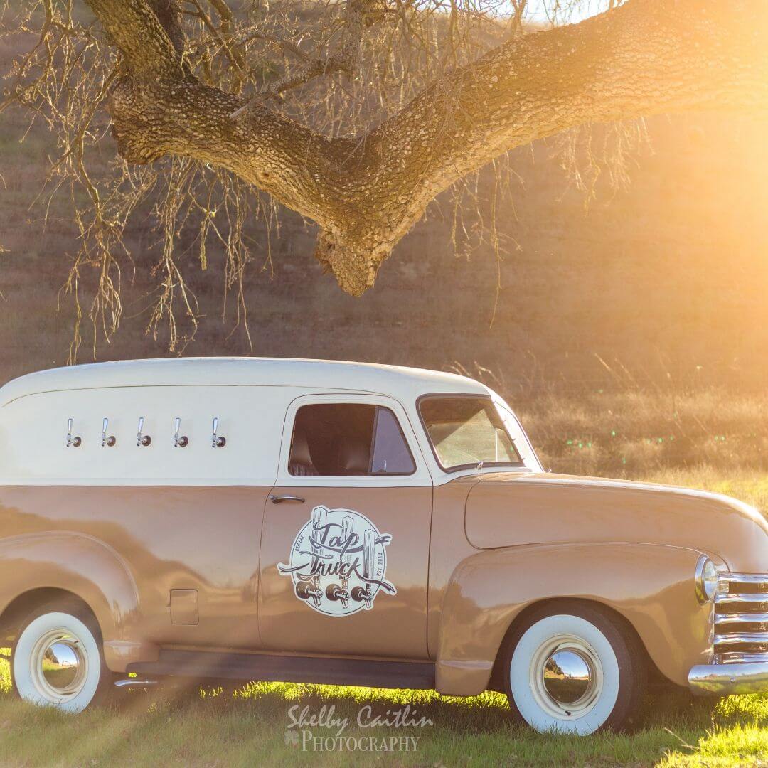 White truck and wedding gown with bride and groom at outdoor venue.  