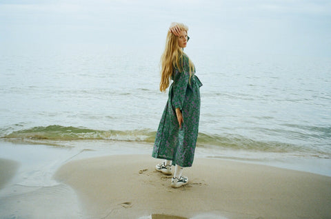 Lily wears a teal silk robe on a beach with sneakers