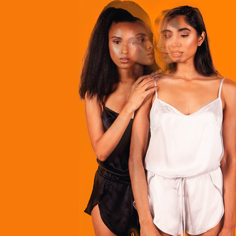 Kent Woman Silk Romper in Black and Cloud Gray, shown on two different models, front view, on orange background