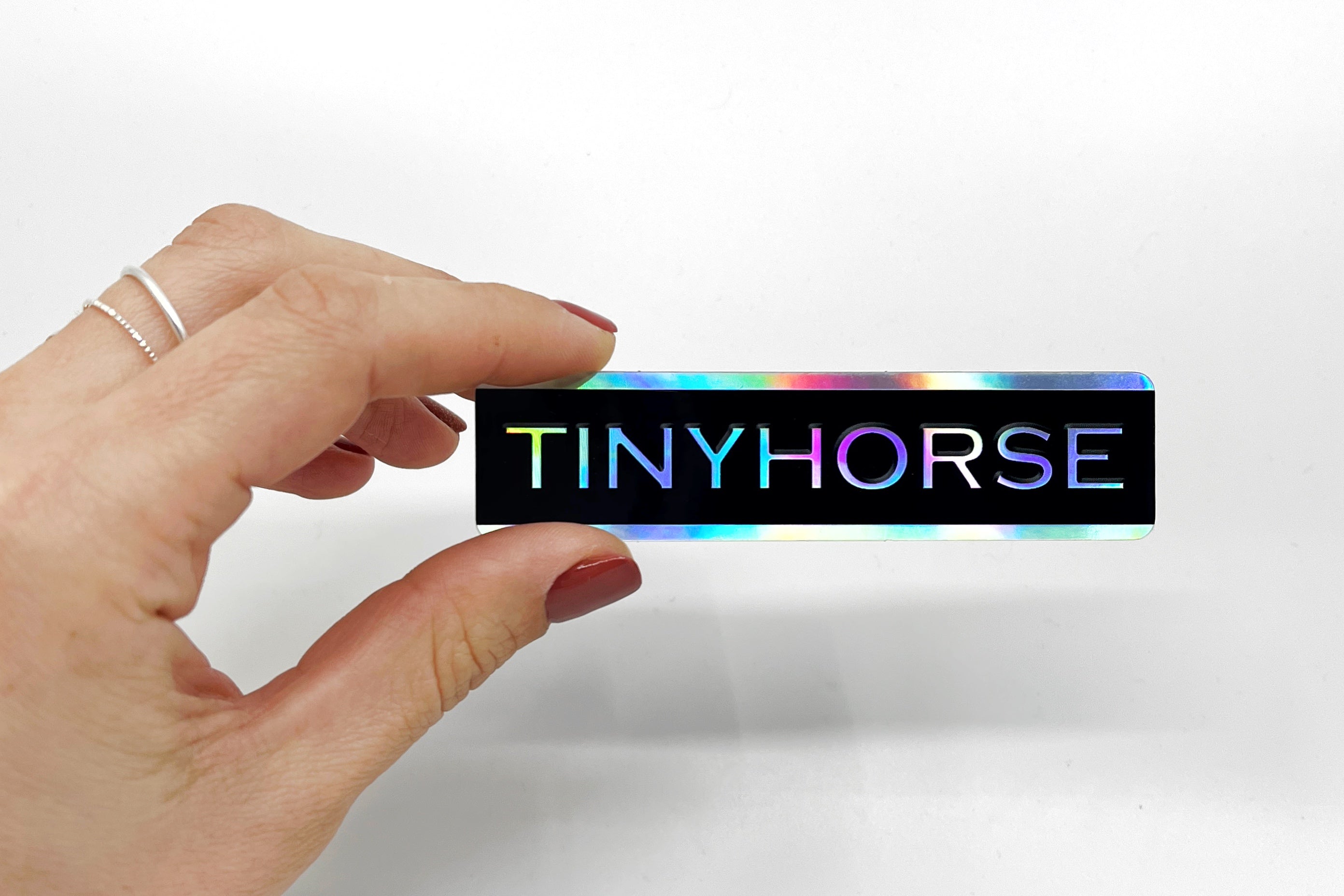 Hand holds a colourful sticker that says “TinyHorse”