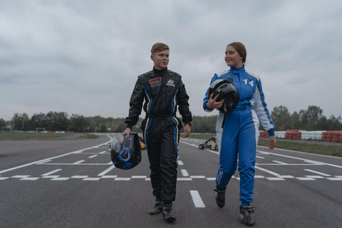 Two people on the racing track wearing racing suits, carrying their helmets