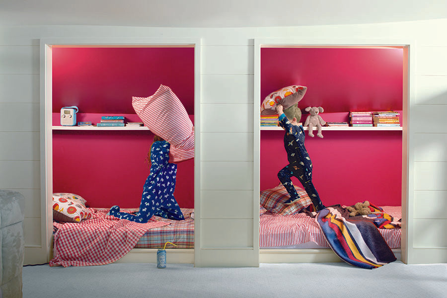 A kid's bedroom painted green and pink, showing two children having a pillow fight.