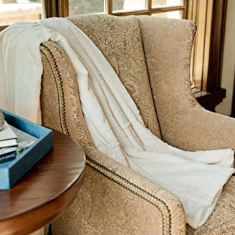 A beautiful Saranoni Luxury home throw blanket draped over an artisan arm chair.