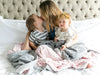 A mother with 2 kids on her laps and they are wrapped in blankets