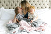A mother with 2 kids on her laps and they are wrapped in blankets