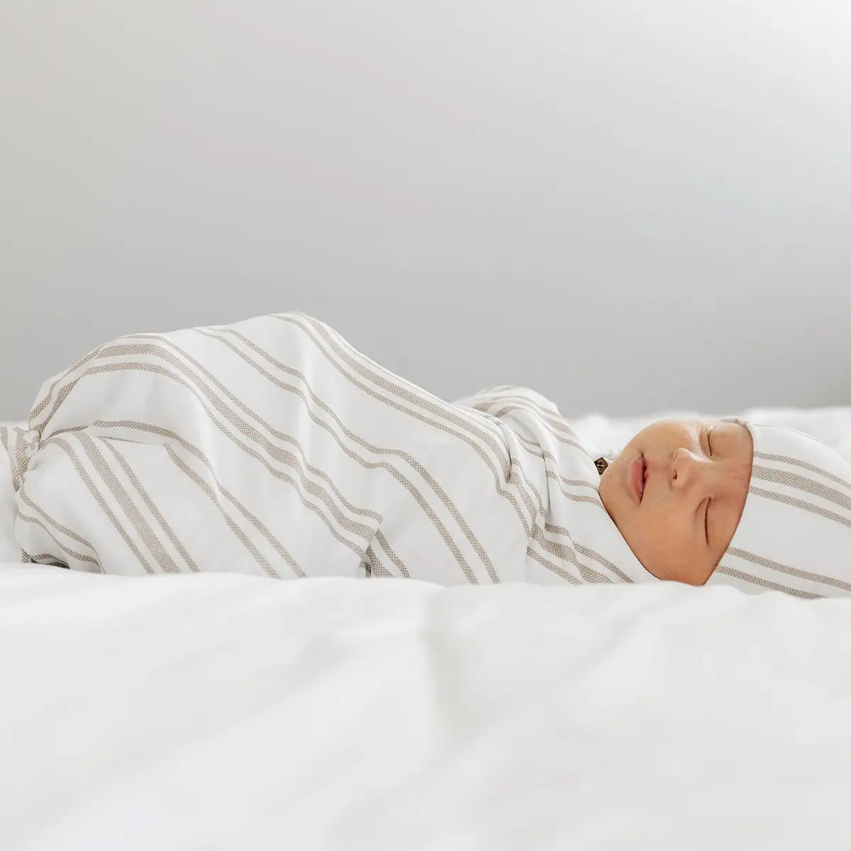 Newborn boy peacefully sleeping on a bed, wrapped in a cozy striped blanket.
