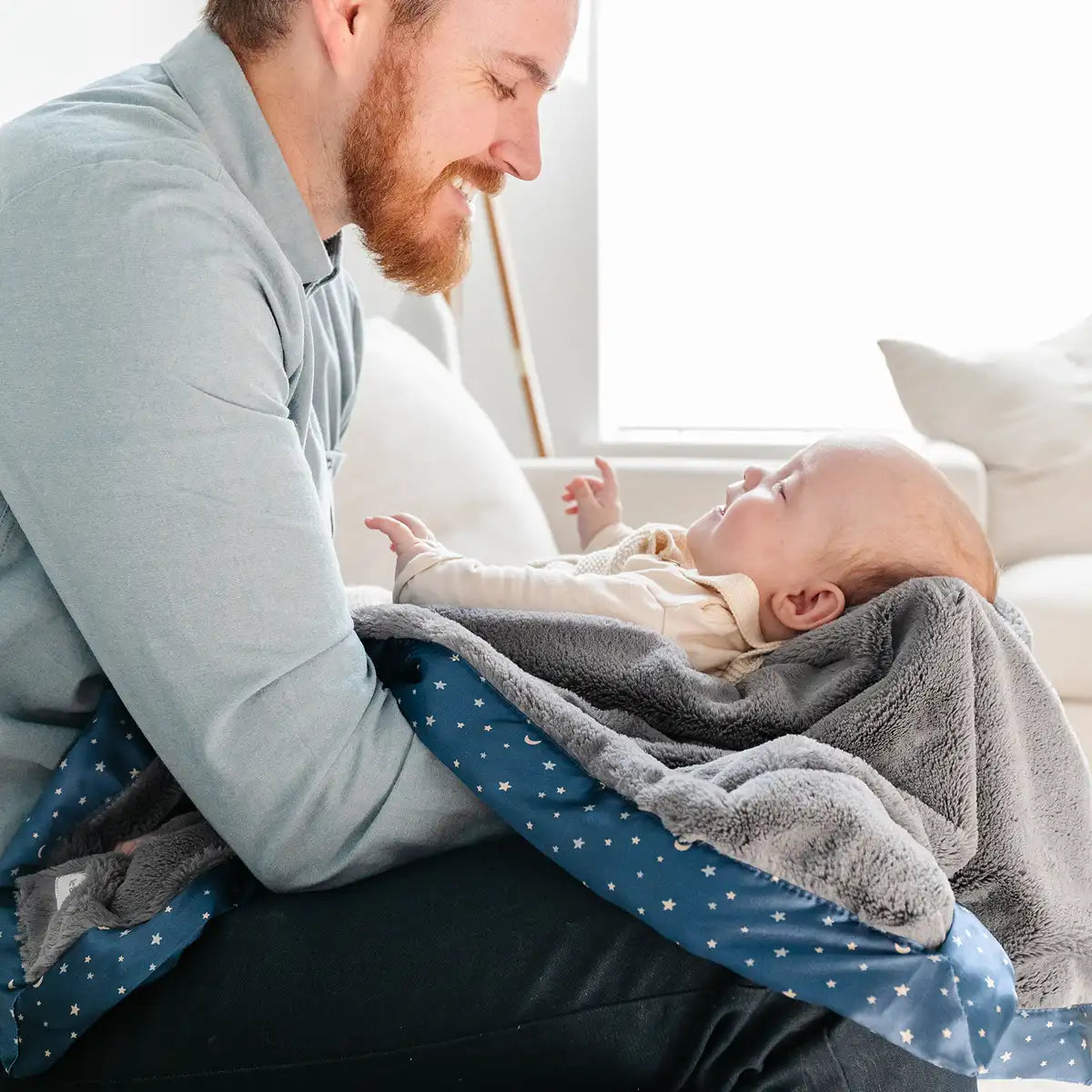 A man gently holds a baby wrapped in a soft blue blanket, smiling warmly at the camera.