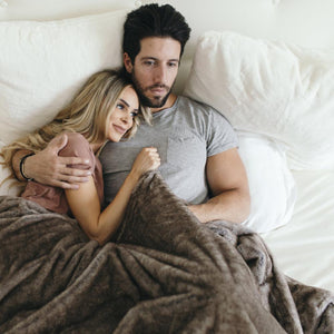 Man and women cuddled in a luxury bedding set with brown tones and made of faux fur. 