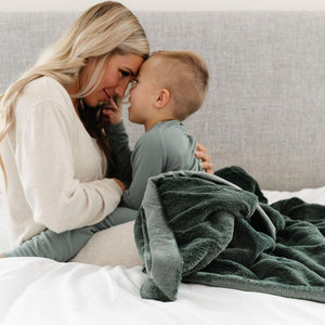 A mother and son lay under a dark green blanket for toddlers and teens.