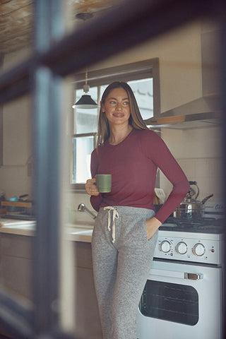 woman in a red long sleeve shirt with a built in bra by SheBird is leaning against a white oven while holding a coffee mug