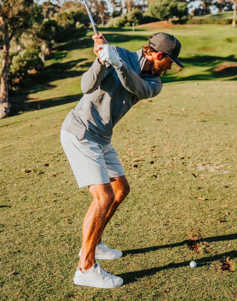 Golfer swinging golf club wearing performance quarter-zip layer
