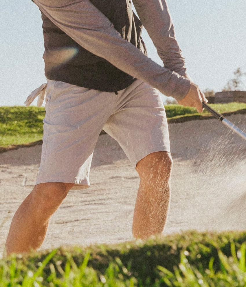 Man swinging golf club in bunker wearing Linksoul Performance Golf Shorts