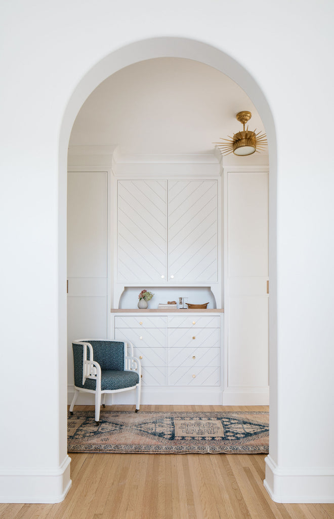 white curved archway leading to white closet cabinets with chair and rug