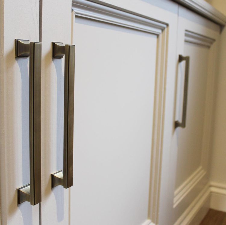 close up of antique brass cabinet pull handles on neutral painted cupboards