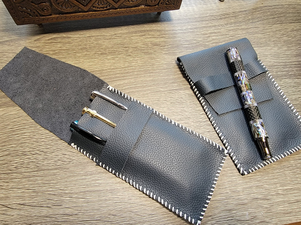 Two leather pouches, one open holding three fountain pens, one closed with a pen on top of it