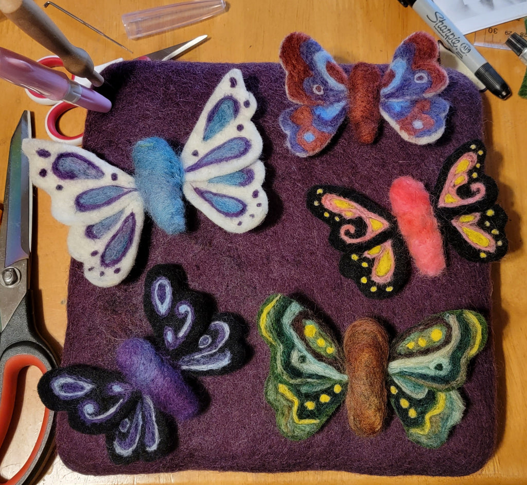 Five needle felted butterflies on a purple felting mat