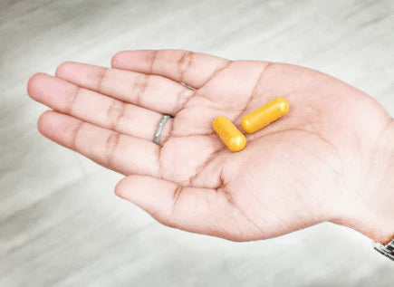 Hand holding two yellow capsules on an open palm.