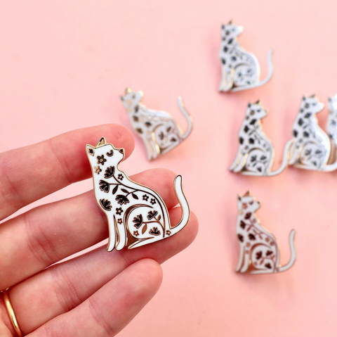 A hand holding a cat enamel pin