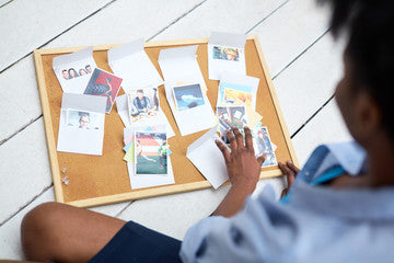 woman sitting on ground pinning print-out pictures to a cork board 