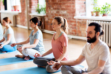group of men and woman on the floor sitting criss-cross doing yoga
