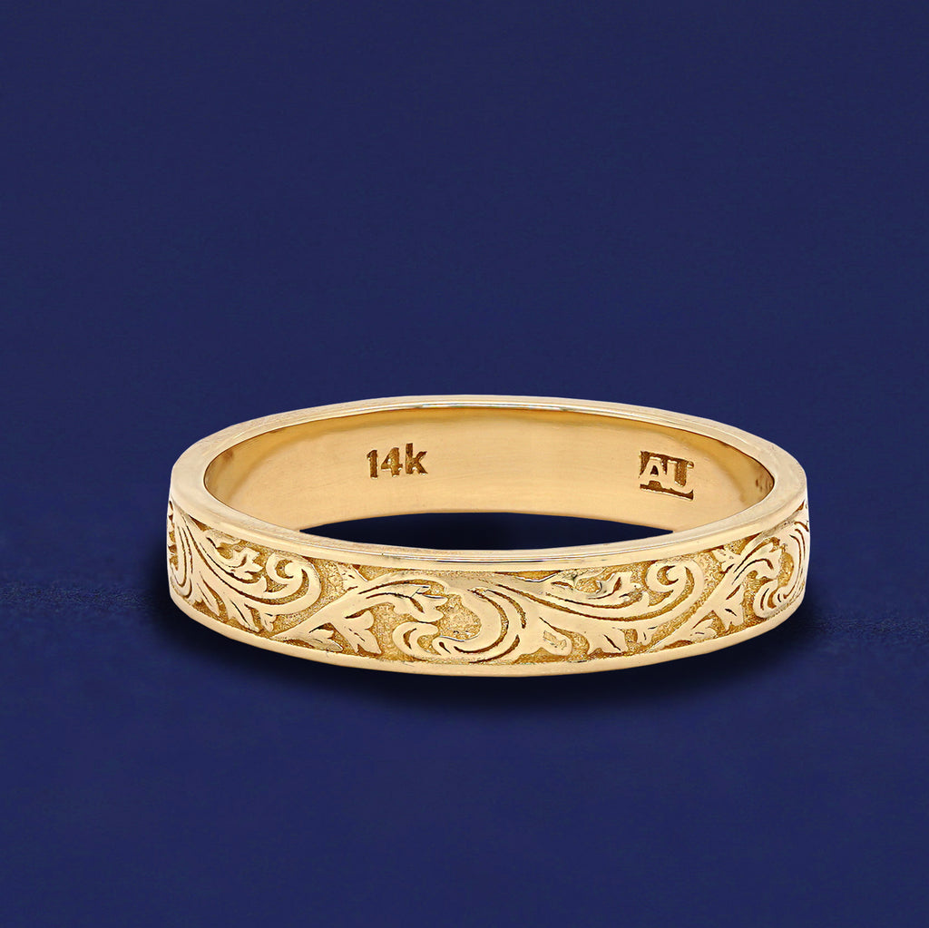 A solid 14k yellow gold filigree wedding band on a dark blue background