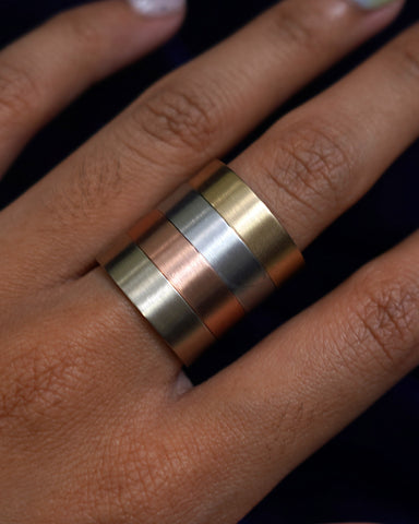 A model's hand wearing a stack of four wedding bands in yellow, white, rose and champagne gold